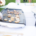 Plan serré sur des brochettes de crevettes en train de cuire à la plancha, lors d’un mariage champêtre à Fréjus. Une animation culinaire signée par un traiteur événementiel du Var.