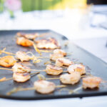 Plan serré sur des brochettes de crevettes en train de cuire à la plancha, lors d’un mariage champêtre à Fréjus. Une animation culinaire signée par un traiteur événementiel du Var.